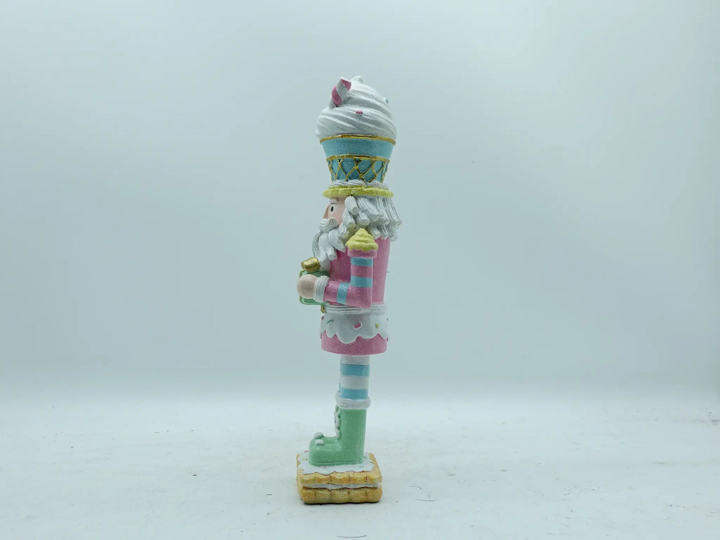 A decorative nutcracker figurine painted in pastel colors, standing on a light gray background, left side view .