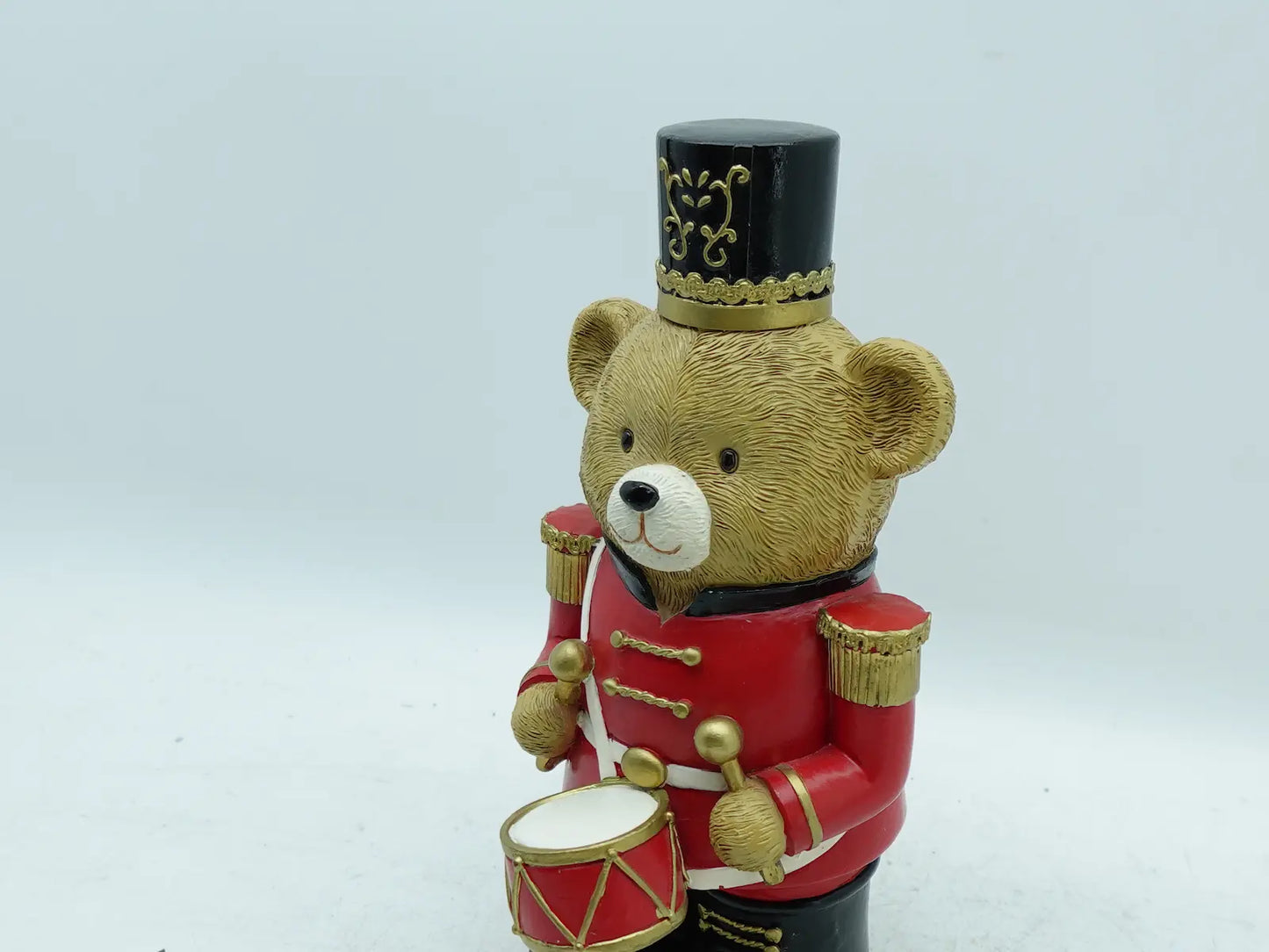 Close-up detail of the red uniform teddy bear drummer figurine showing facial features, top hat emblem, and drumsticks