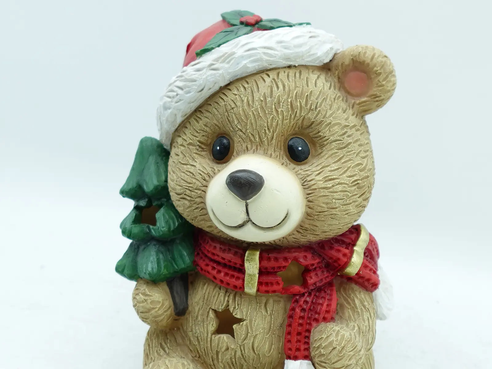 the teddy bear fiigurine's face showing the holly-trimmed Santa hat, textured fur, and star-cutout scarf, close-up detail