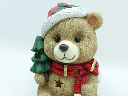 the teddy bear fiigurine's face showing the holly-trimmed Santa hat, textured fur, and star-cutout scarf, close-up detail