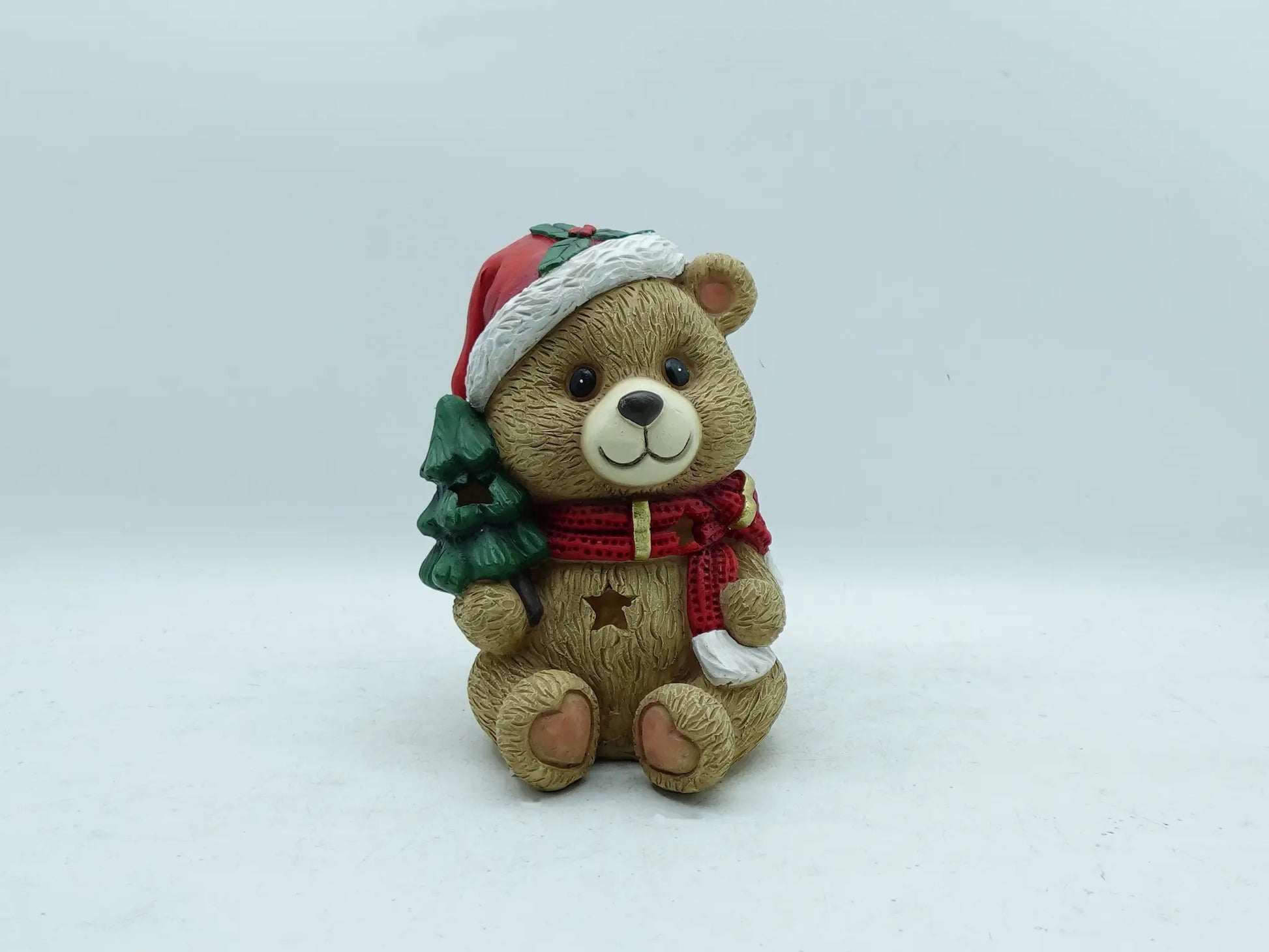 A teddy bear Christmas ornament figurine in tan, holding a small green Christmas tree.