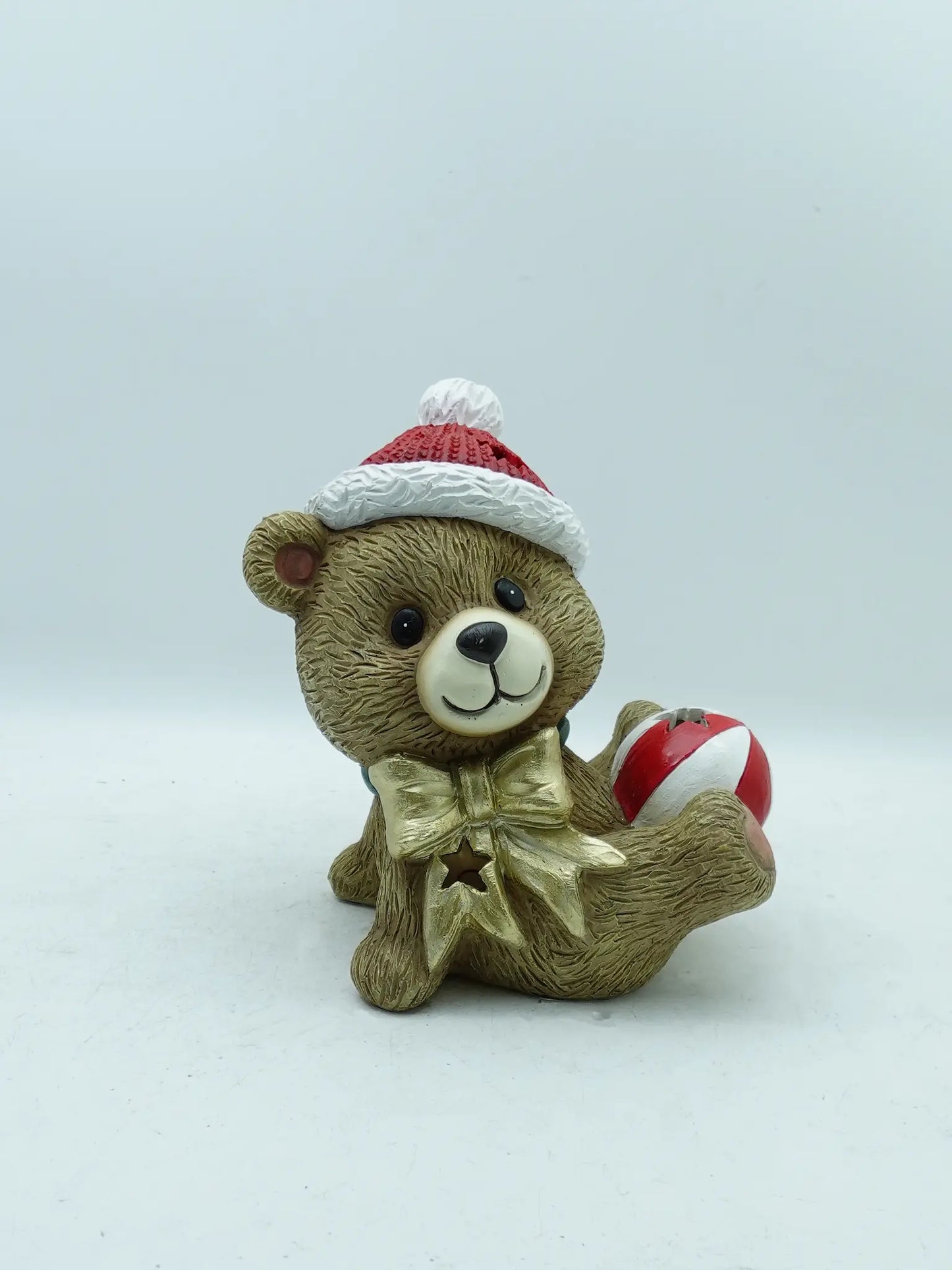 a playful Christmas teddy bear figurine lying down, holding the striped Christmas bauble on white background