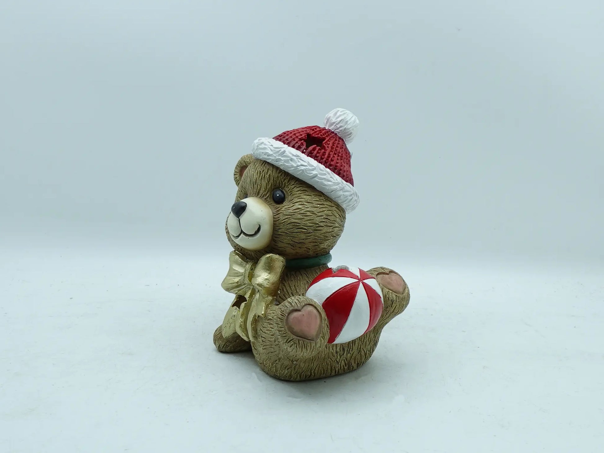 the playful teddy bear figurine lying down, holding the striped Christmas bauble on plain background