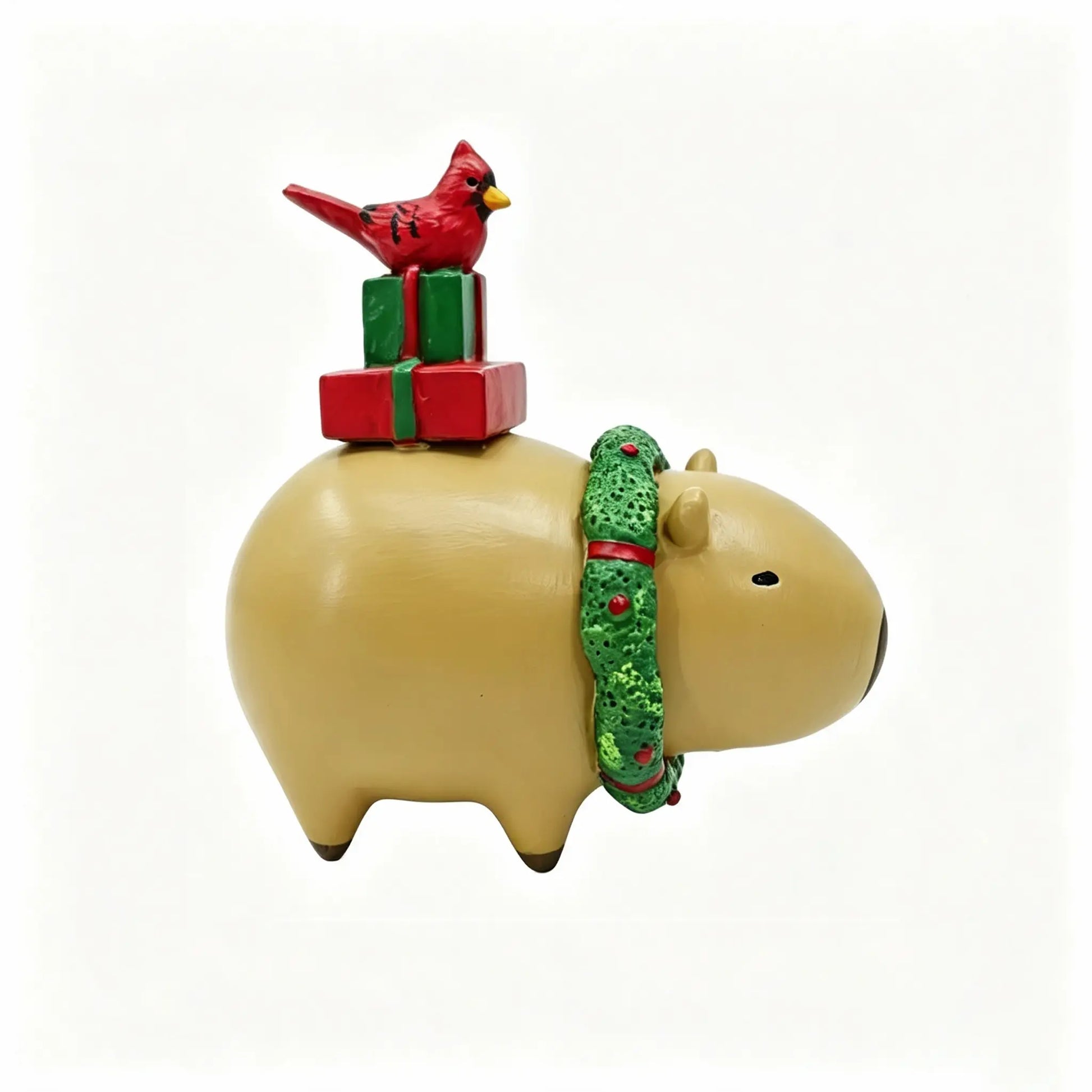 Hand-painted Christmas capybara figurine with green wreath scarf, stacked red and green gift boxes, and red cardinal bird on white background