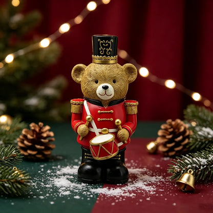 the red teddy bear drummer figurine displayed among pine branches, pine cones, fairy lights, and artificial snow