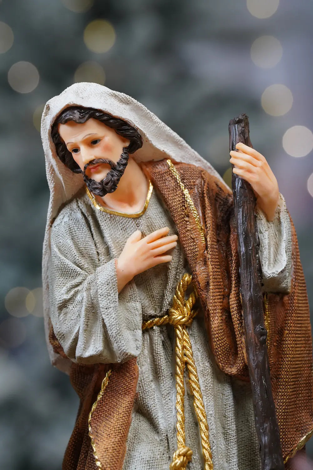 Joseph nativity figurine close-up — linen and brown textile-texture robes with gold cord and hand-over-heart devotional pose