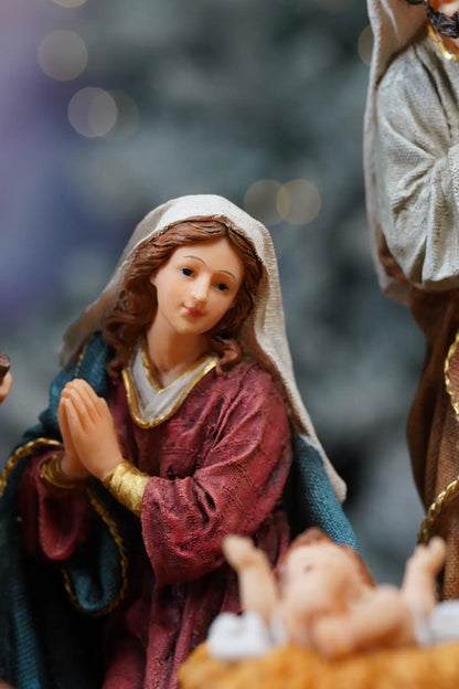 Virgin Mary nativity figurine close-up — kneeling Madonna in deep crimson robe with teal mantle and gold bracelet beside Baby Jesus manger