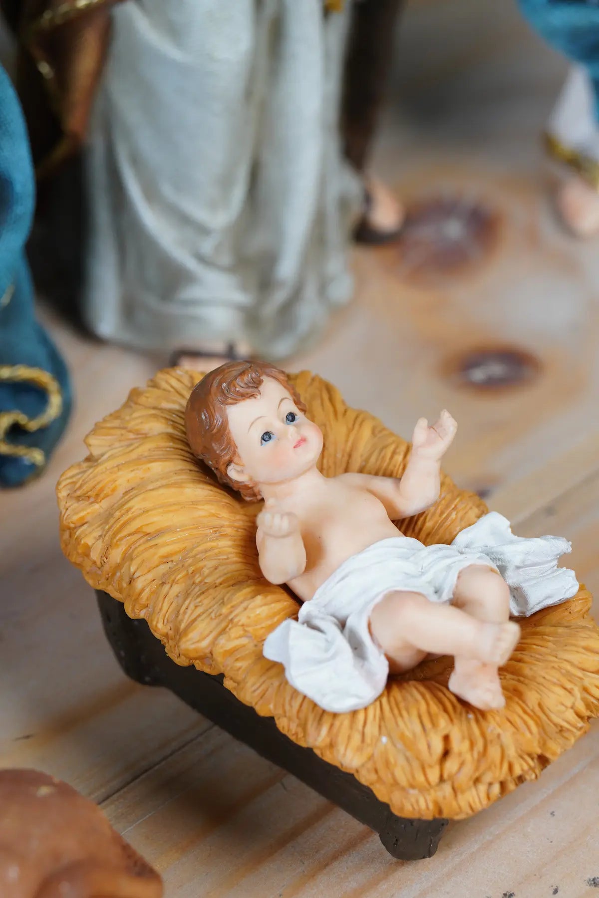 Baby Jesus nativity figurine close-up — infant with blue eyes in golden straw manger on rustic wood surface