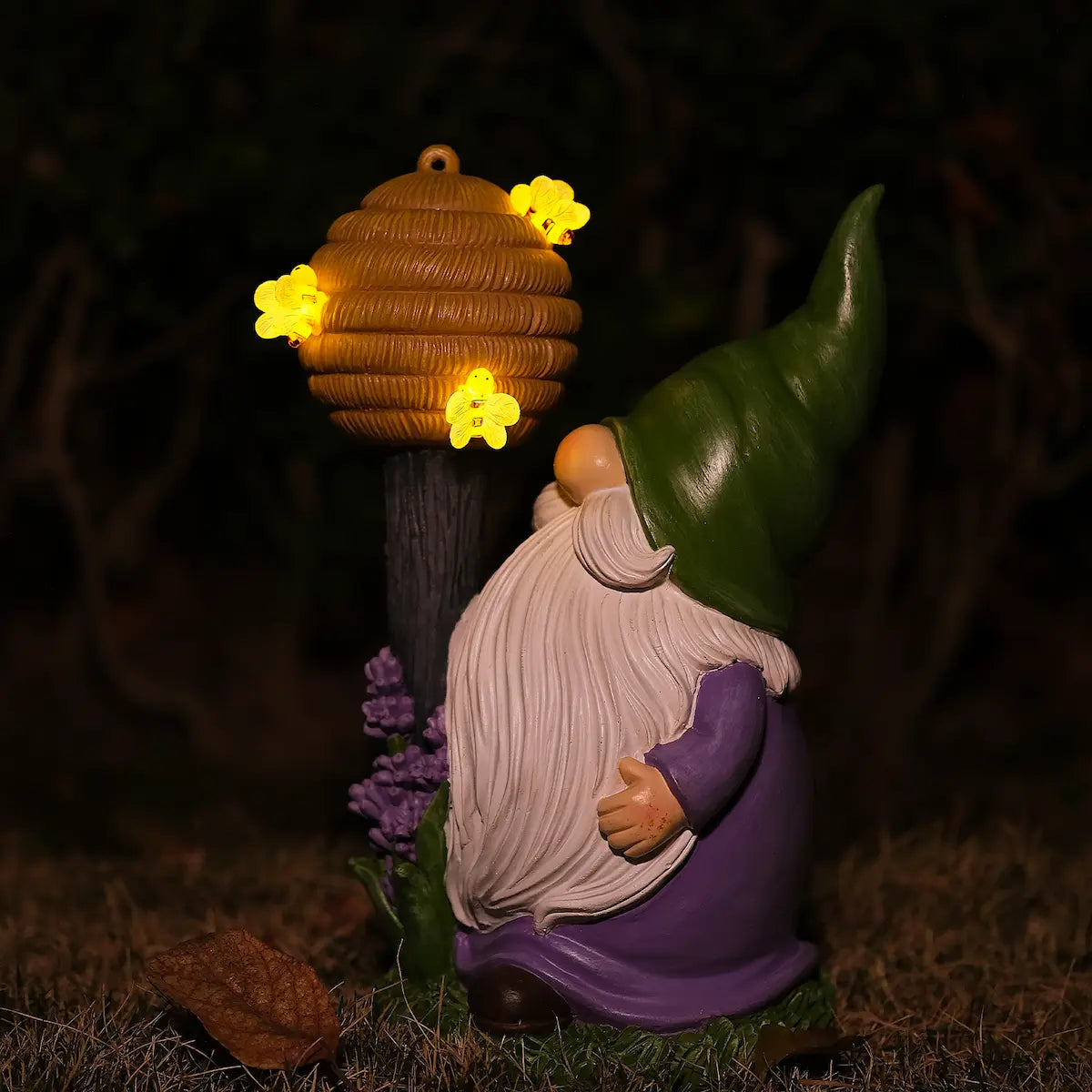 Night view of lighted bee gnome statue with beehive staff and warm LED bee lights