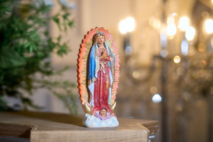 Religious Virgin Mary statue with golden rays displayed near greenery and candlelight