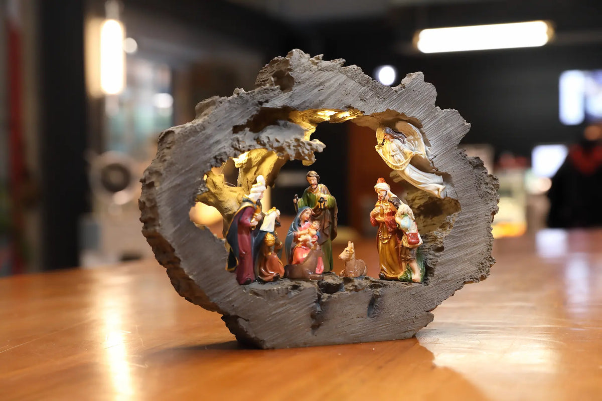 Zayton lighted nativity scene in rustic log stable, set on a wooden tabletop with a blurred indoor background.