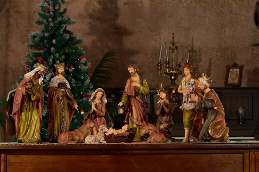 Complete nativity scene with kneeling angel displayed on sideboard in candlelit room with Christmas tree