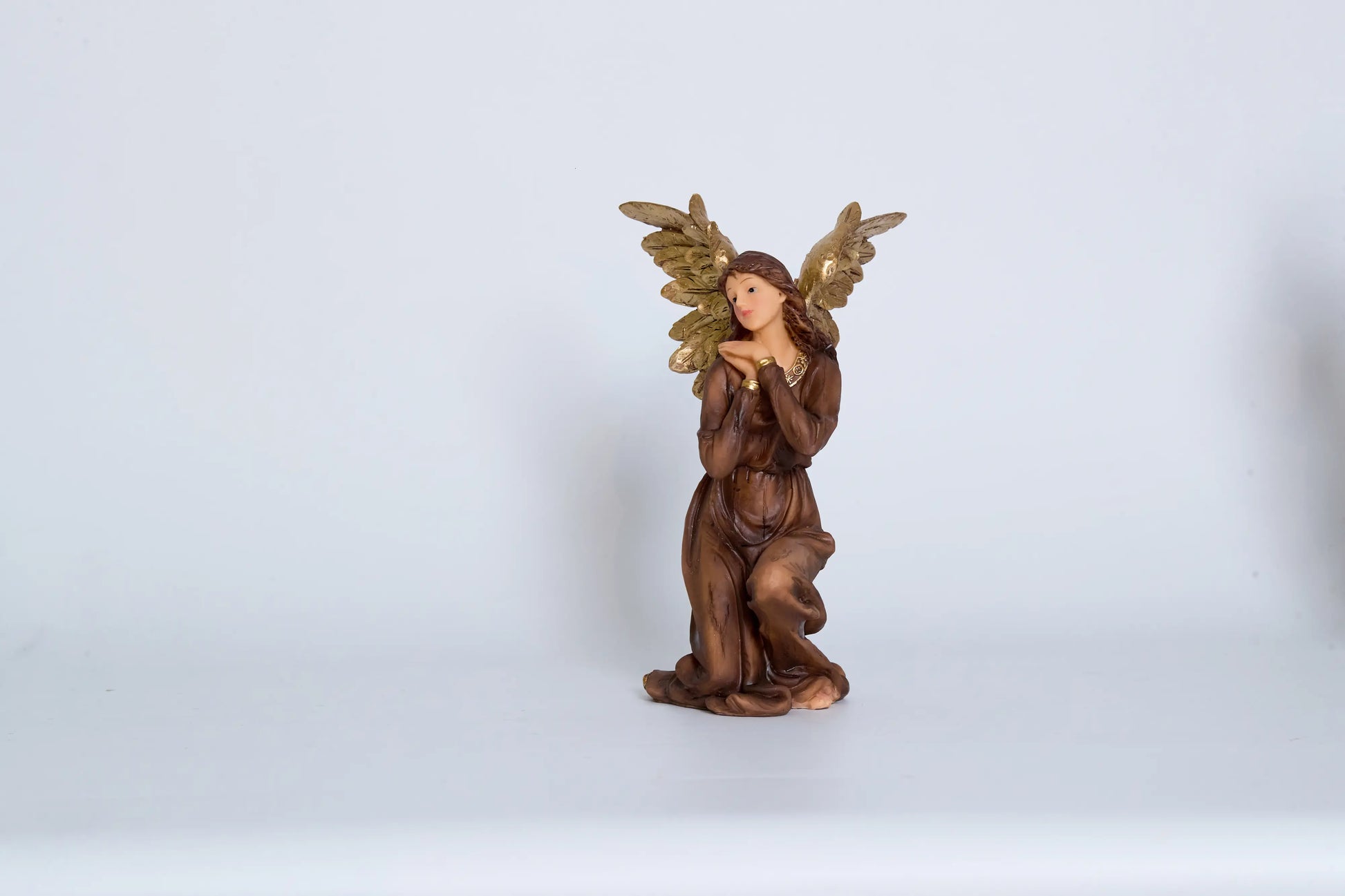Kneeling angel nativity figurine close-up — hand-painted resin angel in brown robes with raised gold wings in adoration pose