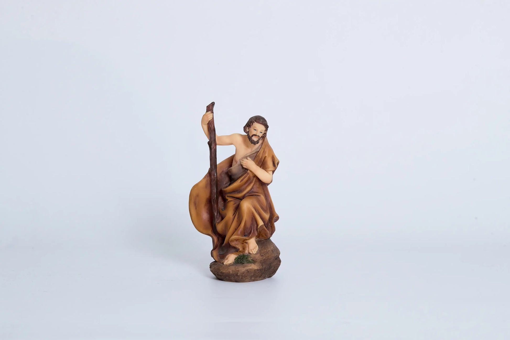 Joseph nativity figurine close-up — seated Saint Joseph in amber robes with wooden walking staff, hand-painted resin crèche figure
