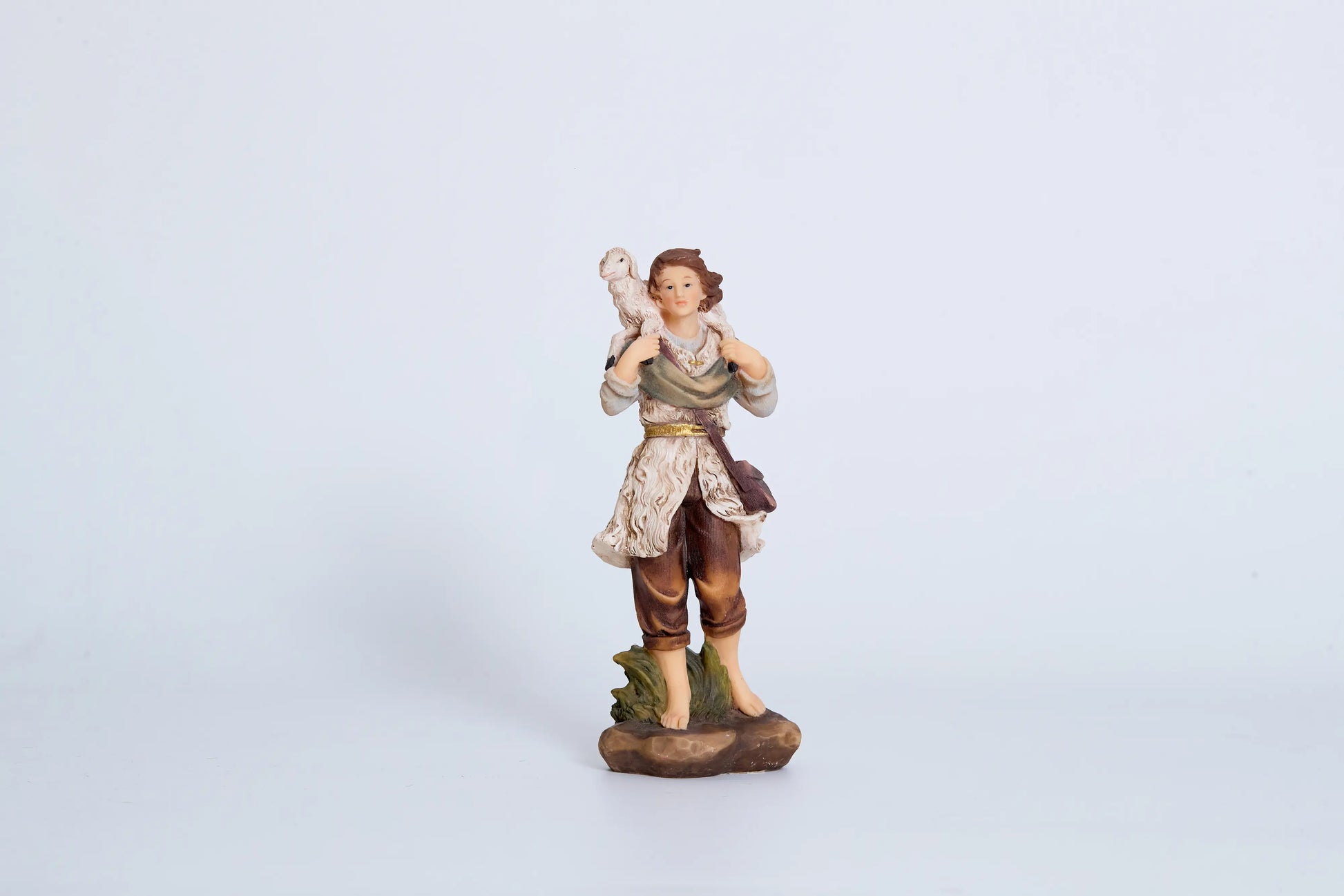 Young shepherd nativity figurine — shepherd boy carrying white lamb on shoulder with gold belt and sheepskin vest, hand-painted resin crèche figure