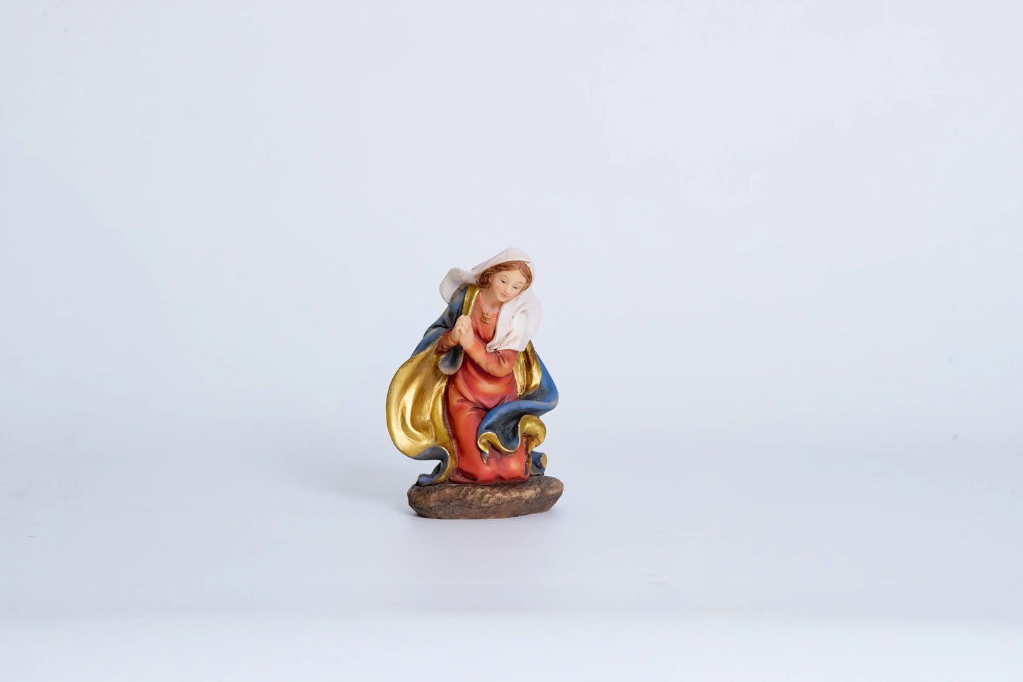 Virgin Mary nativity figurine close-up — kneeling Madonna in crimson robe with blue-and-gold mantle and gold necklace, hand-painted resin devotional figure