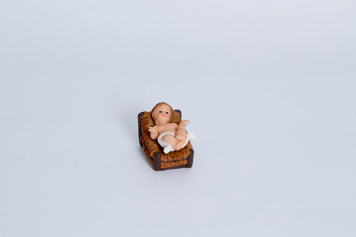 Baby Jesus nativity figurine close-up — infant with blue eyes in woven straw manger, removable resin crèche figure 