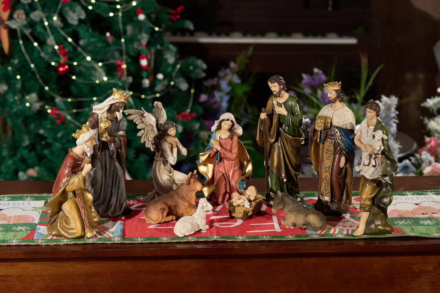 Nativity scene set on wood tabletop with Christmas tree and florals — complete hand-painted resin manger scene