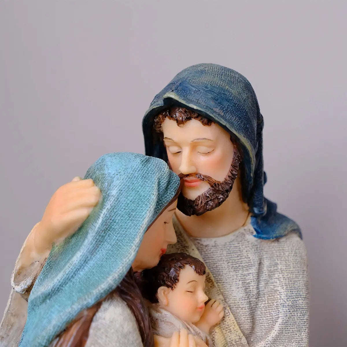 Holy Family figurine close-up of Mary and Joseph's faces embracing above sleeping Baby Jesus, hand-painted resin detail