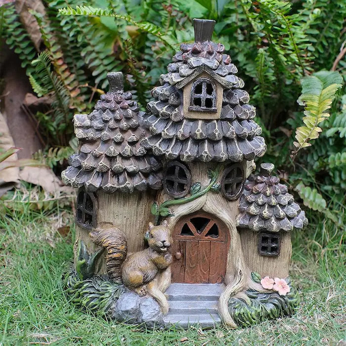 Solar squirrel fairy house displayed in garden with ferns and green grass