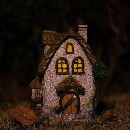 Solar stone fairy house glowing warm yellow light at night in outdoor garden