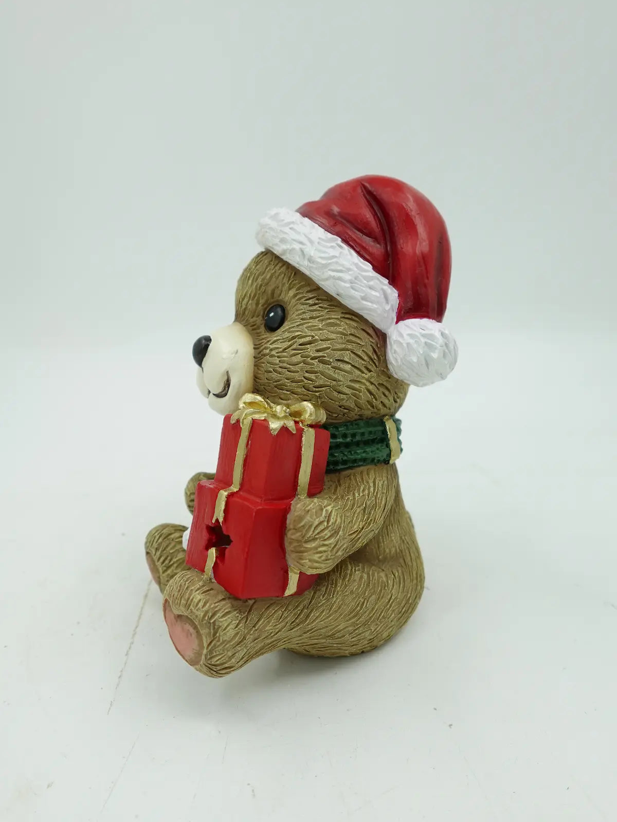 A brown teddy bear figurine, showing the teddy bear's smile, scarf texture, and gift box details