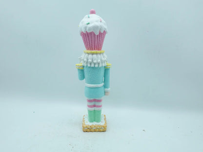 A cupcake-themed nutcracker figurine shown from the back, standing on a small gold base against a plain light gray background.