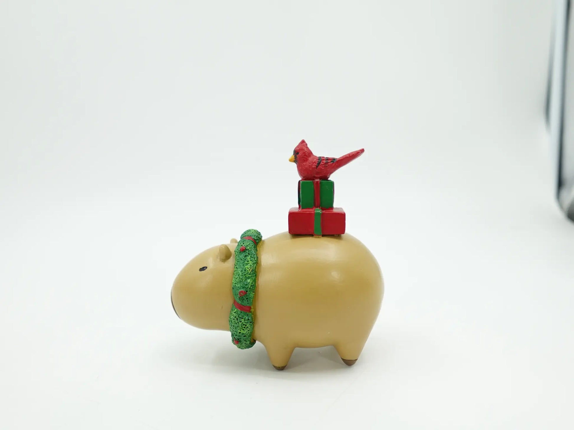 resin Christmas capybara figurine showing the rounded body, green textured scarf, and gift stack with cardinal