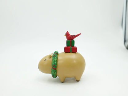 resin Christmas capybara figurine showing the rounded body, green textured scarf, and gift stack with cardinal