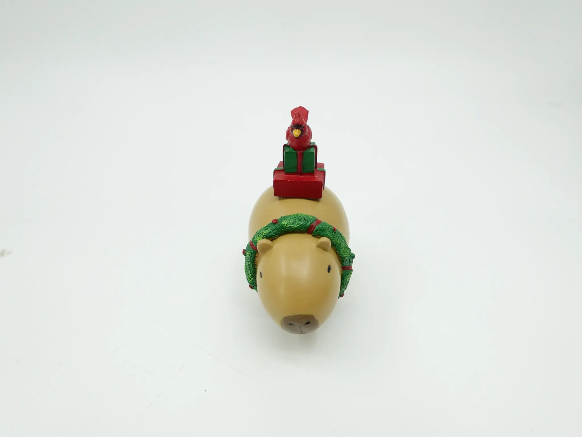 hand-painted capybara figurine facing forward with green wreath collar and stacked presents