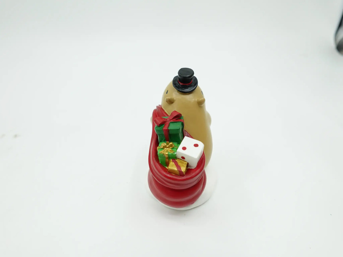 resin Christmas capybara figurine showing the overflowing red sack filled with green, gold, and polka-dot gift boxes, back view