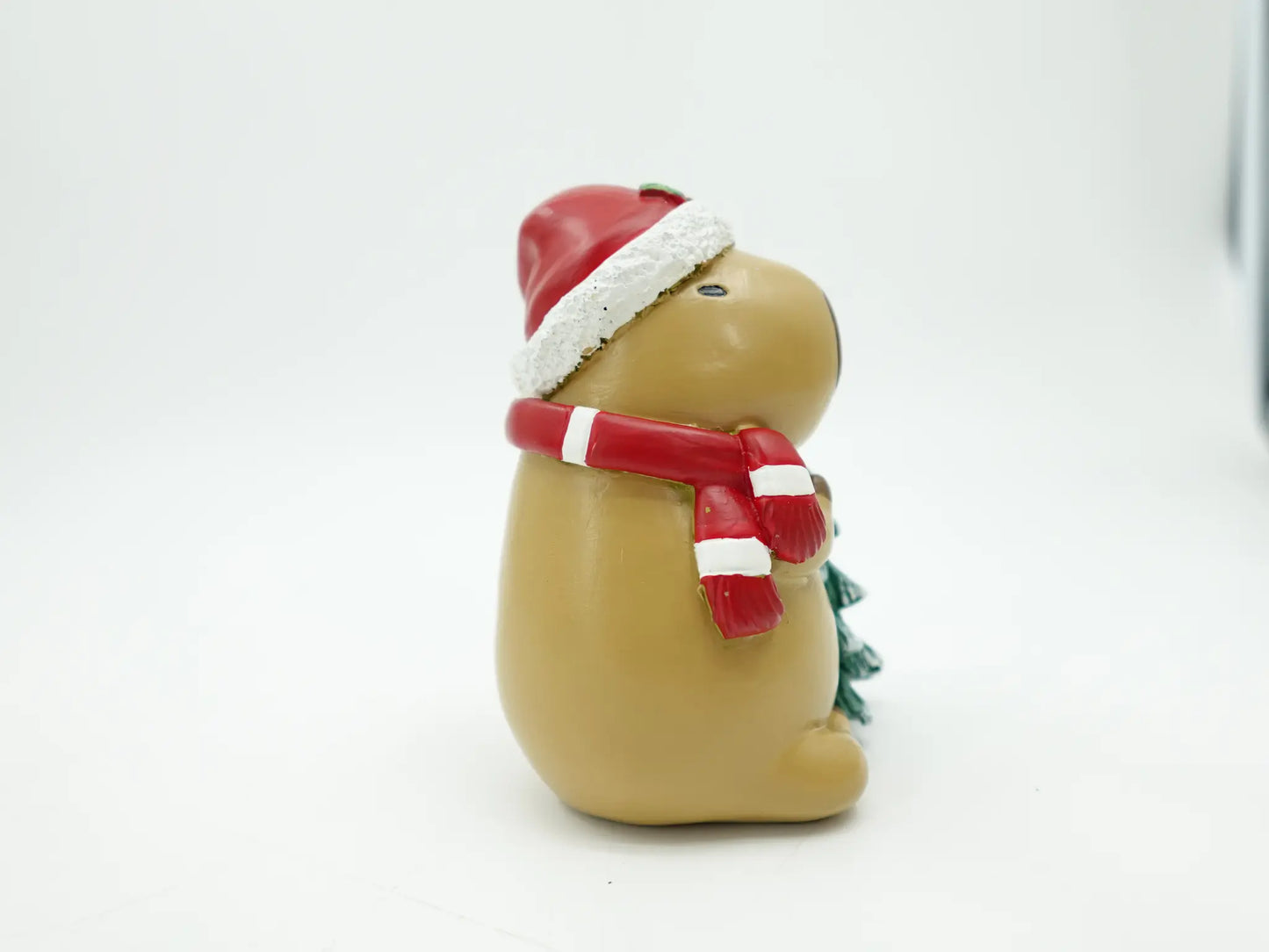the resin capybara figurine showing the Santa hat pom-pom and candy-cane striped scarf, side view