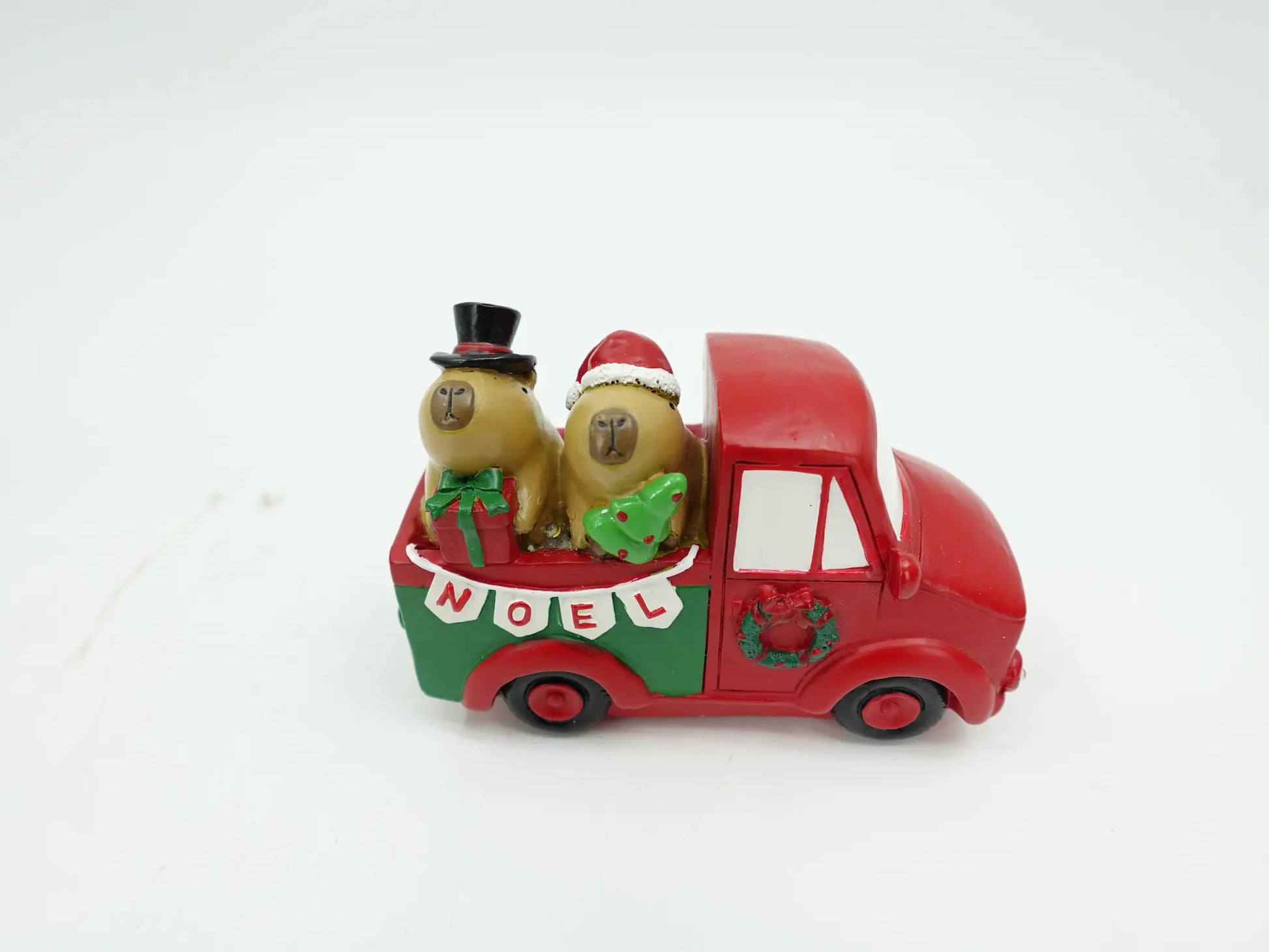 the Christmas capybara couple figurines riding in the truck bed with top hat, Santa hat, gift, and tree