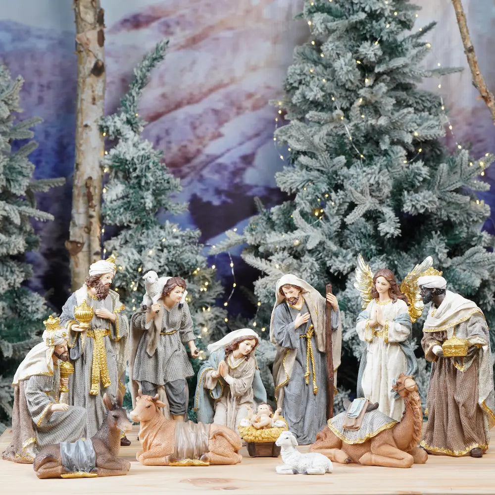 Zayton Christmas nativity set display with multiple figurines, arranged in front of decorated Christmas trees and a scenic backdrop.