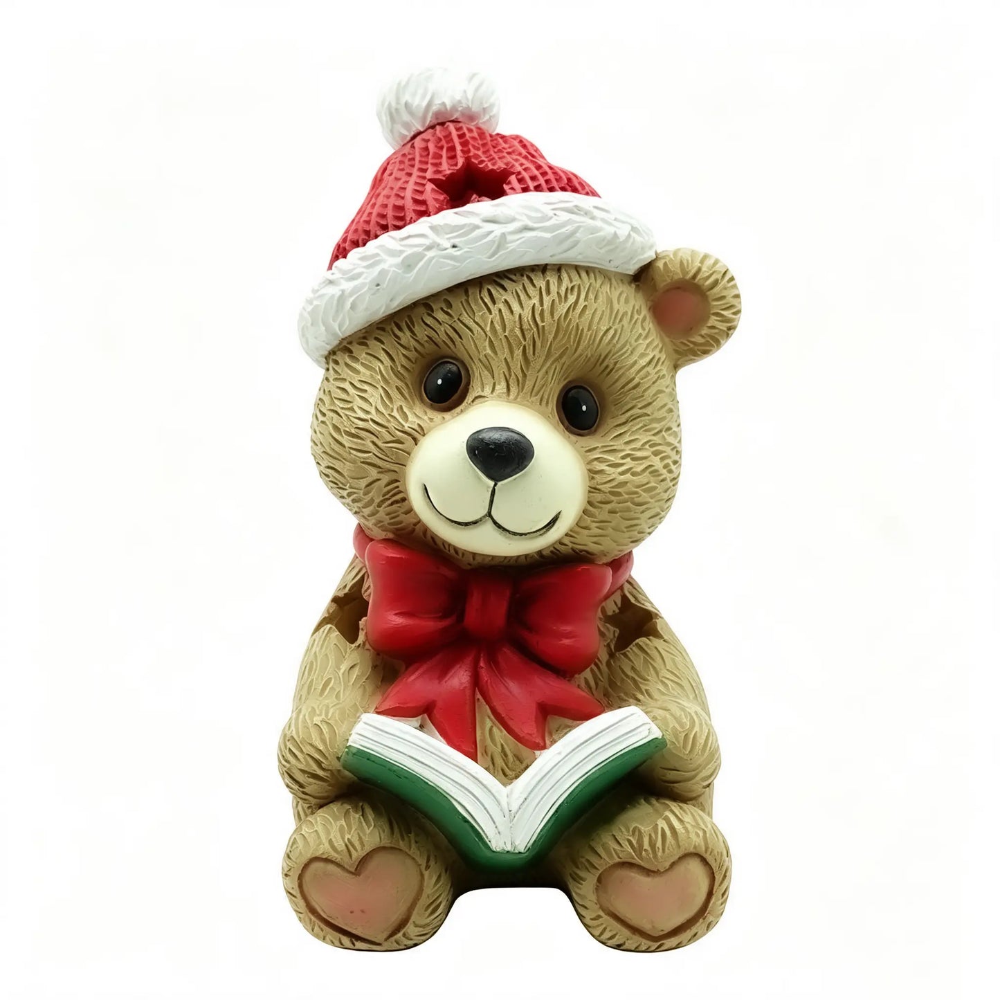 A Christmas teddy bear figurine wearing a red and white Santa hat and a red bow tie, holding an open book with green and white pages, on a plain white background.