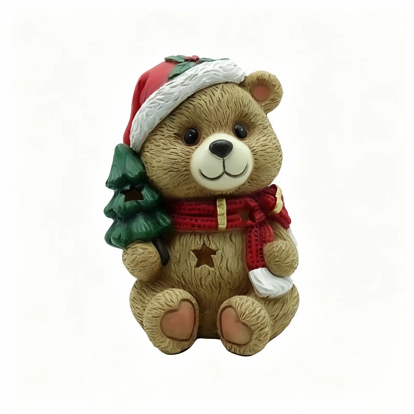 A teddy bear Christmas ornament figurine holding a small green Christmas tree, wearing a Santa hat and a red scarf with gold stars.